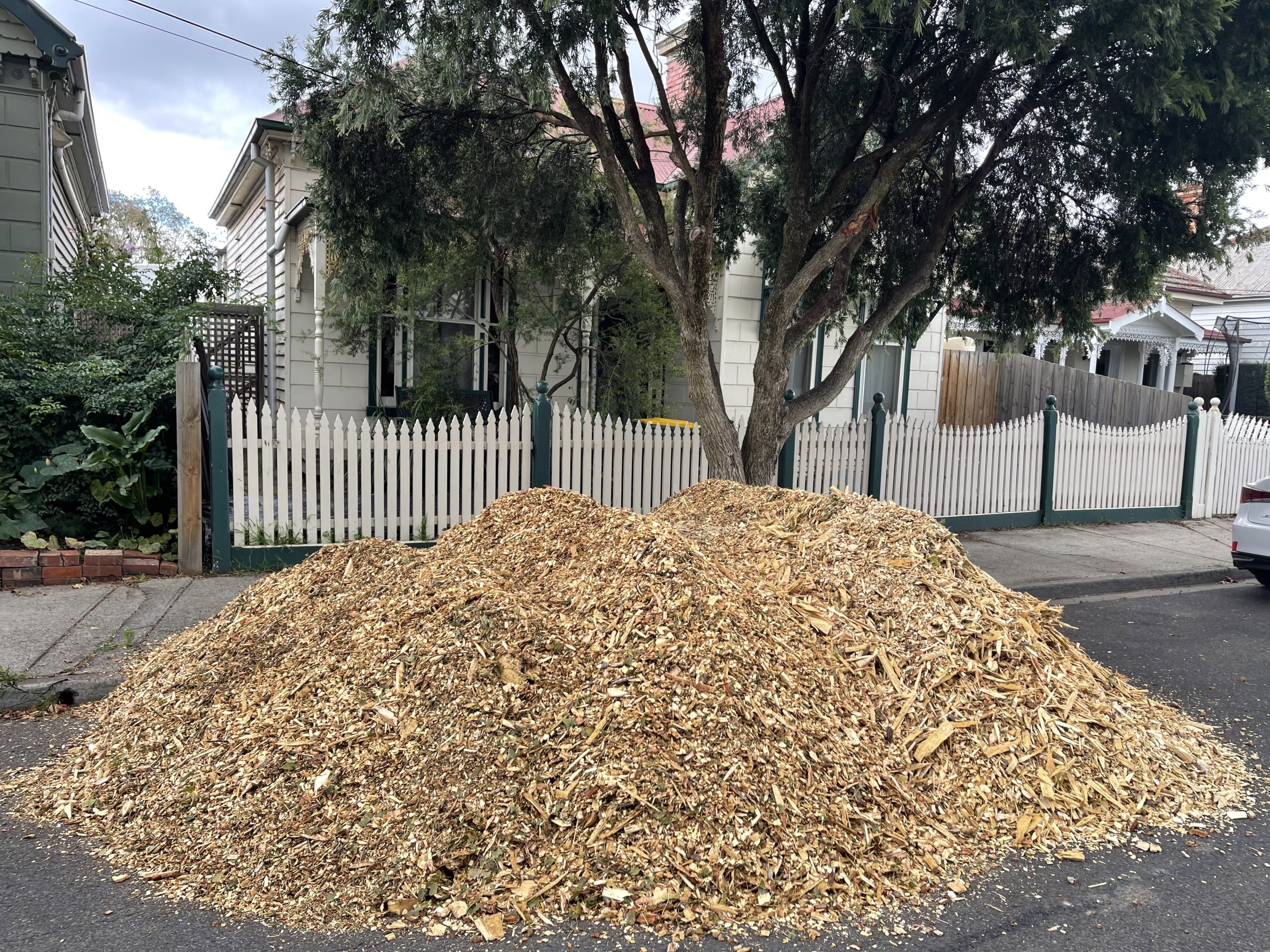 Street-side mulch deliveries beside a suburban picket fence